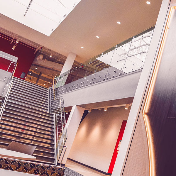 Modern multi-level interior with a staircase, seating area, balconies, and a large illuminated reggie, the redbird head logo wall panel.