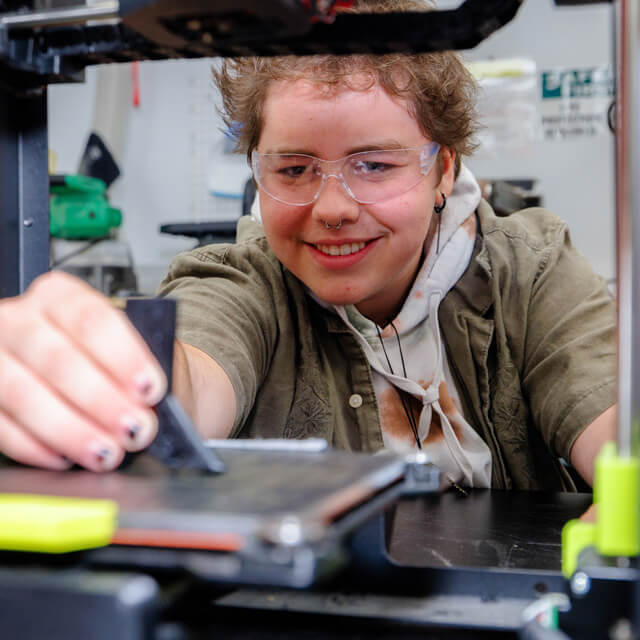 Student pulls a print off of a 3D printer.